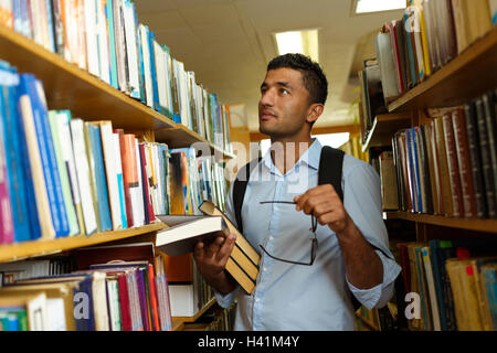 Young arab student reading book between the shelves in the library Stock Photo