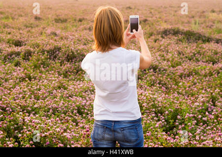 Caucasian woman photographing field of flowers with cell phone Stock Photo