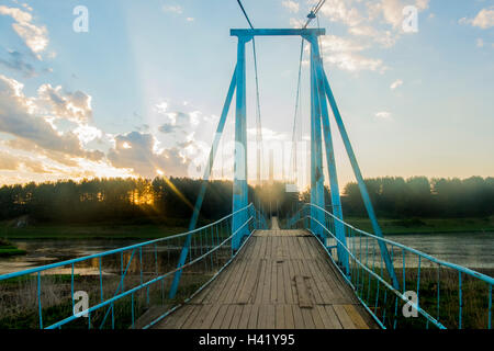 Sunbeams on wooden footbridge over river