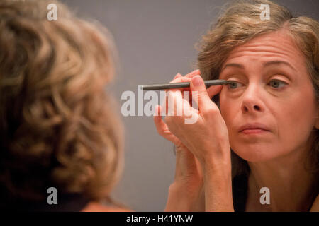 Caucasian woman applying eyeliner in mirror Stock Photo