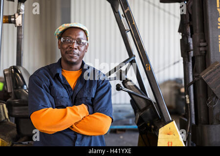 Smiling Black worker posing near forklift in factory Stock Photo