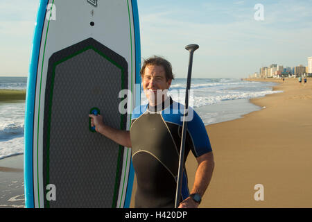 Man posing with paddleboard on beach Stock Photo
