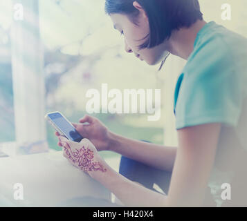 Mixed Race girl texting on cell phone near window Stock Photo