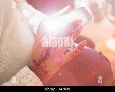 Woman with henna tattoos on hands texting on cell phone Stock Photo