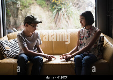 Mixed Race brother and sister playing finger game on sofa near window Stock Photo