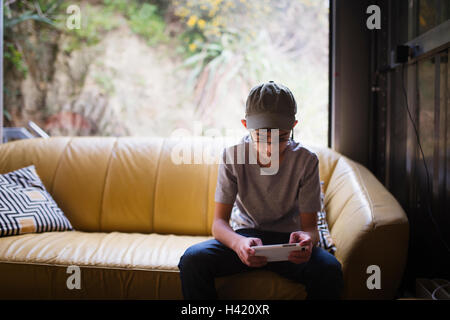 Mixed Race boy sitting on sofa near window texting on cell phone Stock Photo