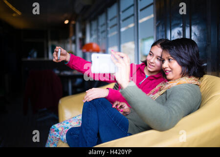 Mother and daughter sitting on sofa posing for cell phone selfie Stock Photo