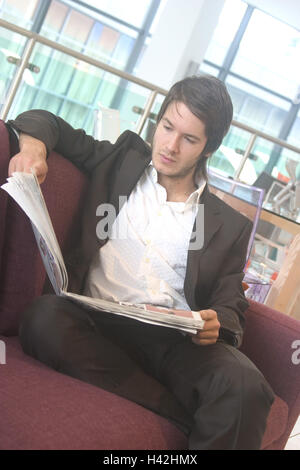 Sofa, man, young, newspaper, reading, 20-30 years, dark-haired, hairstyle, fashionably, calmness, elegant, suit, interest, information, messages, read, newspaper, newspaper, business, inside, at home, loft, flat, flatlet, window front Stock Photo