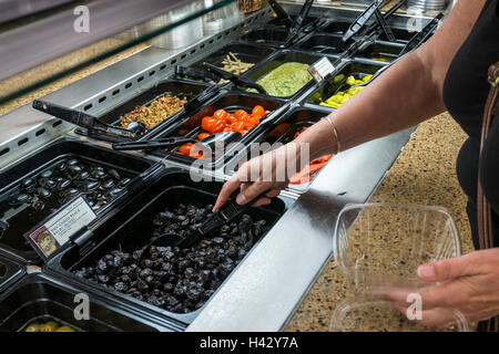 Woman selecting dry-cured black Beldi olives from a supermarket self-service delicatessen counter. Stock Photo