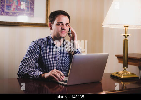 Young happy man talking on the phone at his workplace in office Stock Photo