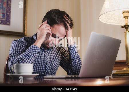 tired man with laptop and coffee having a work call on his phone, businessman in office or home Stock Photo