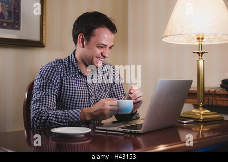 Handsome man drinking coffee in office while typing on laptop Stock Photo
