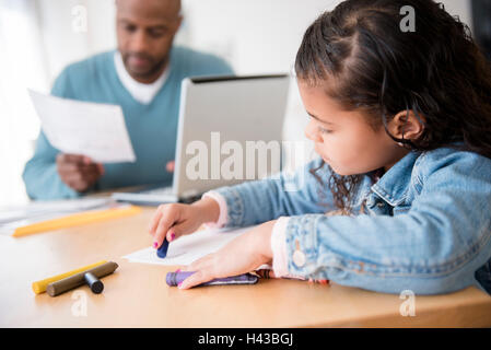 Daughter coloring with crayons while father uses laptop Stock Photo