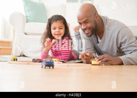 Father and daughter playing with toy cars on floor Stock Photo