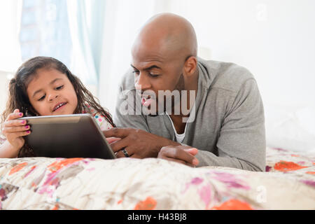 Father and daughter using digital tablet on bed Stock Photo