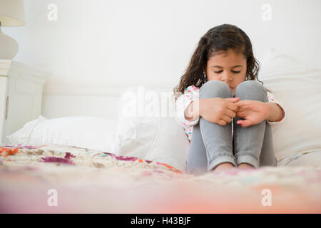 Unhappy Mixed Race girl sitting on bed Stock Photo