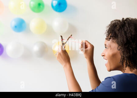 Black woman aiming slingshot at balloons on wall Stock Photo