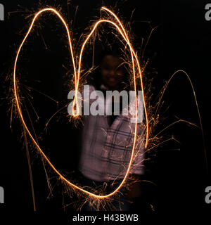 Mixed Race girl making heart-shape with sparkler Stock Photo