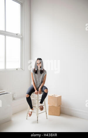 Mixed Race woman sitting on stool in corner Stock Photo