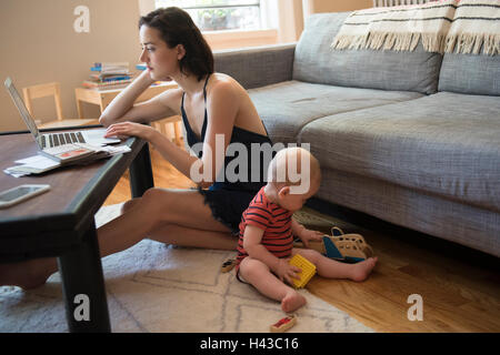 Caucasian mother sitting on floor using laptop near baby son Stock Photo
