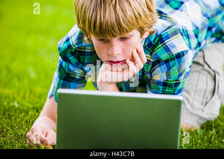 Caucasian boy kneeling in grass using laptop Stock Photo