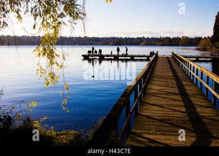 Distant people at end of dock at river Stock Photo