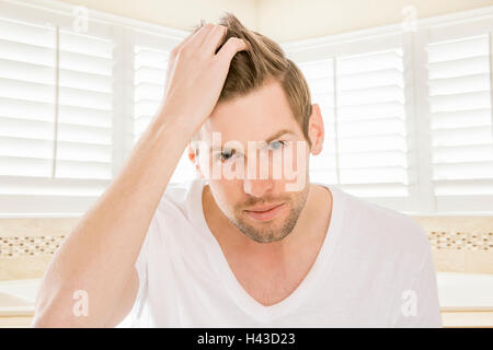 Serious Caucasian man styling hair in bathroom Stock Photo