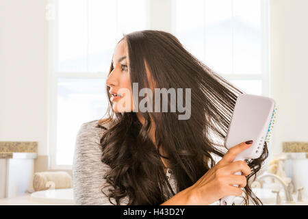 Mixed Race woman brushing hair in bathroom Stock Photo
