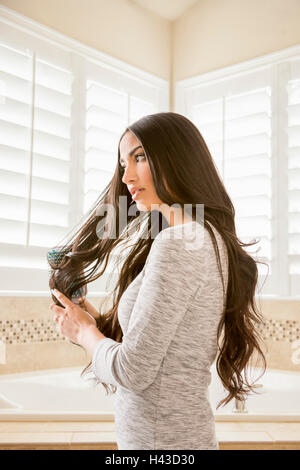 Mixed Race woman brushing hair in bathroom Stock Photo