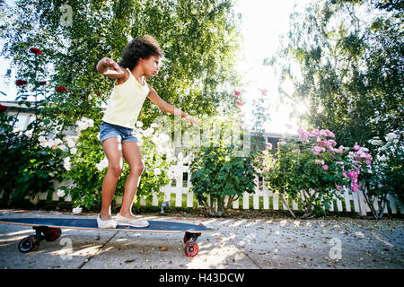 Mixed Race girl skateboarding on sidewalk Stock Photo