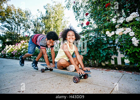 Mixed Race boy pushing sister on skateboard on sidewalk Stock Photo