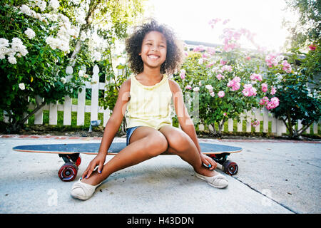 Smiling Mixed Race girl sitting on skateboard Stock Photo