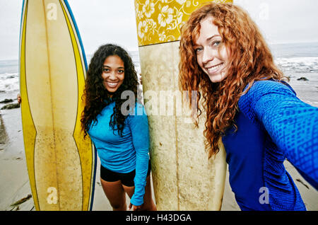 Smiling women holding surfboards posing for selfie at beach Stock Photo