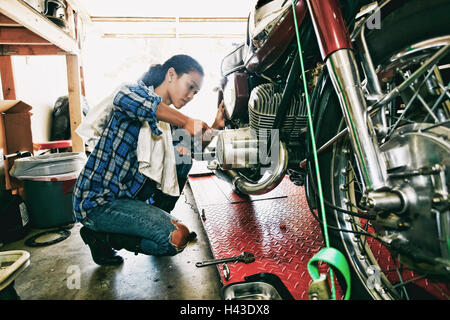 Mixed Race woman repairing motorcycle in garage Stock Photo