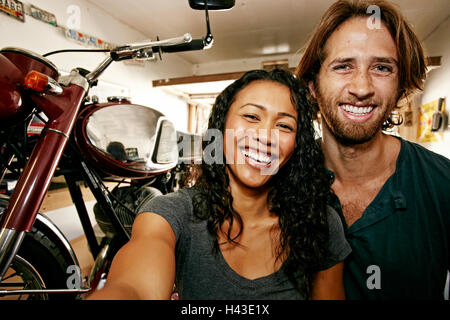 Man and woman posing for selfie with motorcycle in garage Stock Photo