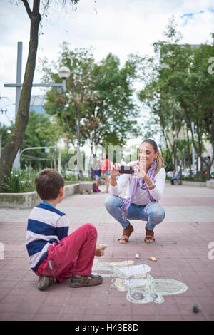 Hispanic mother photographing son on sidewalk Stock Photo