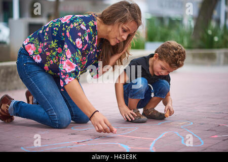 Hispanic mother and son drawing on sidewalk with chalk Stock Photo