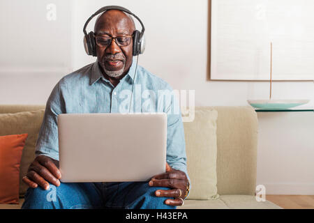 Man sitting on sofa listening to laptop with headphones Stock Photo