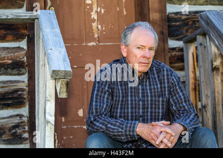 Serious Caucasian man sitting on wooden front stoop Stock Photo