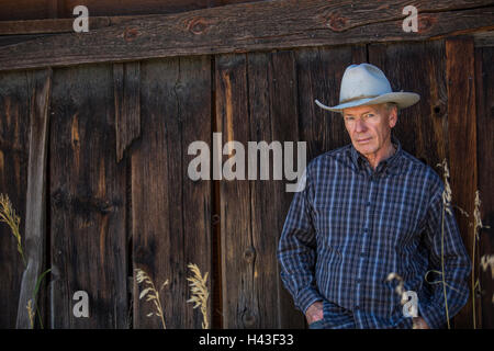 Serious Caucasian farmer leaning on wooden fence Stock Photo