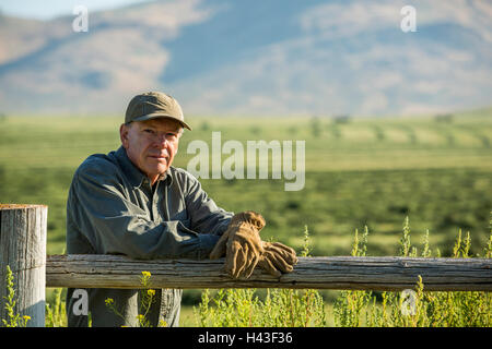 Caucasian farmer wearing gloves leaning on wooden fence Stock Photo