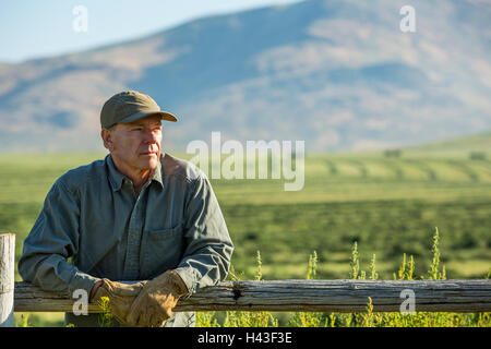 Caucasian farmer wearing gloves leaning on wooden fence Stock Photo