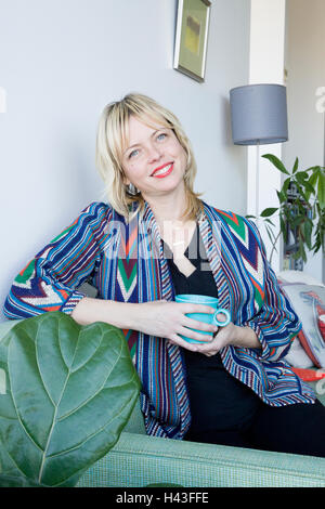 Caucasian woman sitting on sofa drinking coffee Stock Photo