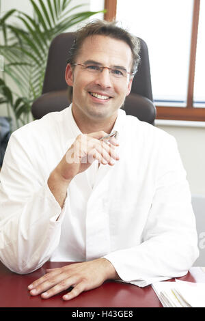 Doctor, smiling, holding, friendly, pen, desk, sitting, half portrait, model released, Stock Photo