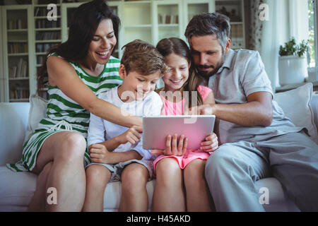 Parents sitting on sofa with their children and using digital tablet in living room Stock Photo