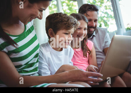 Parents sitting on sofa with their children and using laptop in living room Stock Photo