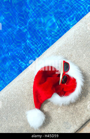 Red christmas hat and sunglasses near the pool. Place for text. Stock Photo