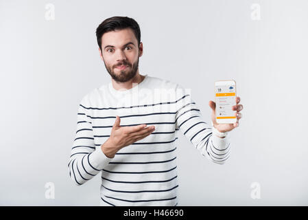 Puzzled bearded man holding and pointing cellphone Stock Photo