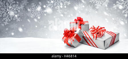 Silver Christmas or birthday gift boxes with red bows in snow, with symbolic snow background, panorama format Stock Photo