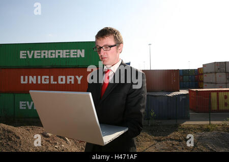 Businessman, seriously, laptop, half portrait, container terminal, containers, logistics, container port, container terminal, business, trade, person, man, glasses, suit, stand, work, communicate thoughtful, intently, data entry, planning, coordination, control, data transmission, e-mail, Internet, Internet connection, communication, WLAN, without cable, notebook computer, computer, portable, mobility, flexibility, transport, cargo, goods, goods traffic, outside, Stock Photo